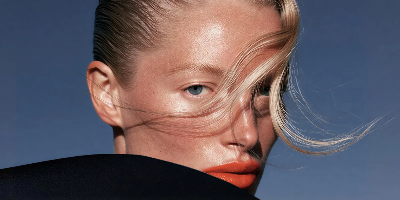 Beauty close-up of a blonde woman with hair across her face and orange lips, the kind of fashion image brands have always retouched