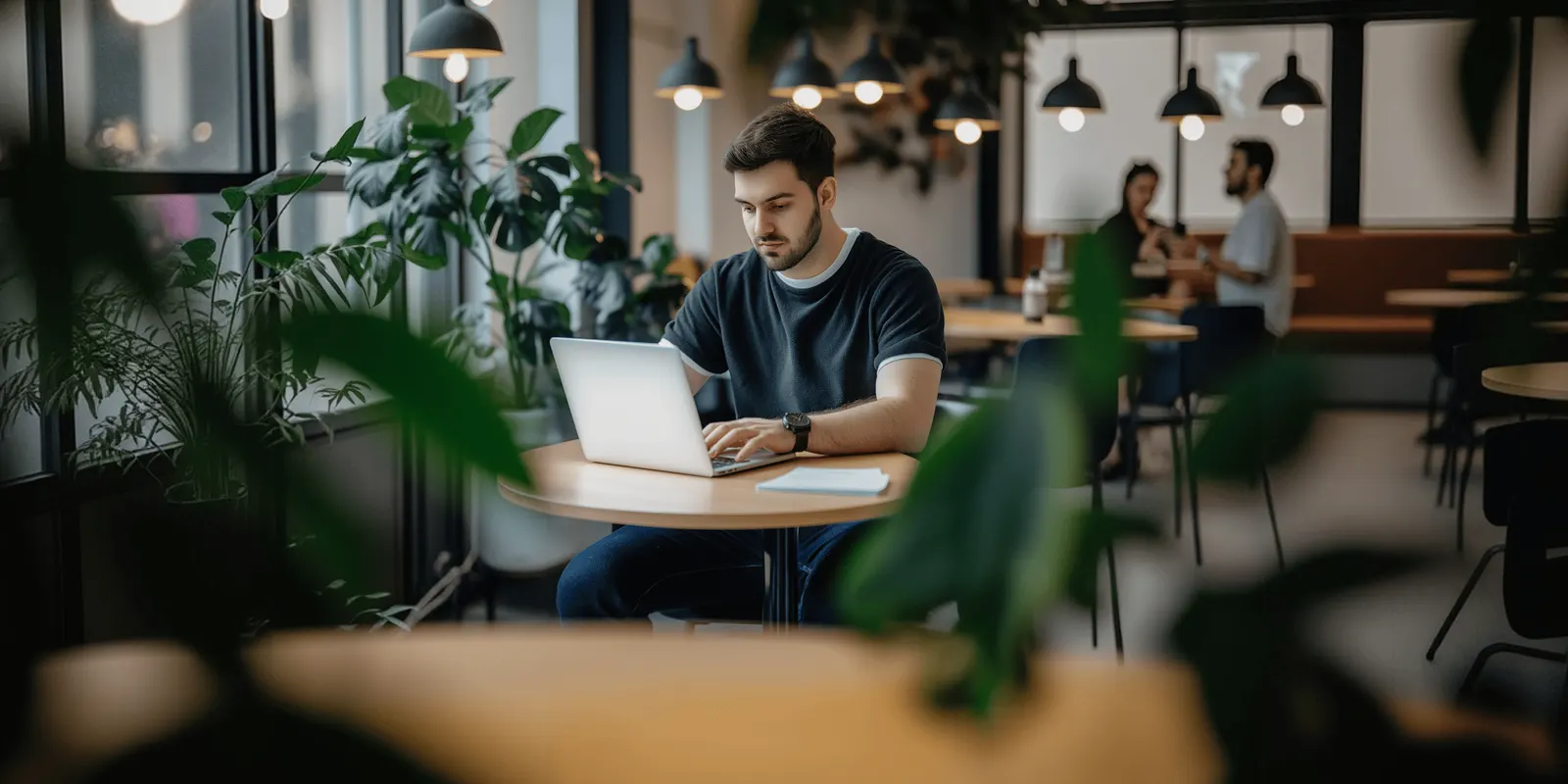 Man types on a laptop at a small cafe table, the writing step where most rejected module copy begins