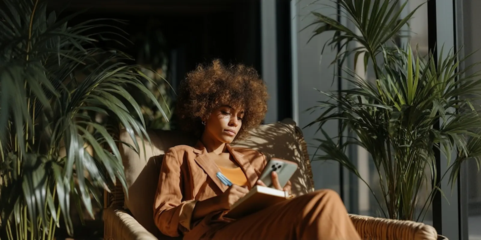 Woman in a tan suit writes in a notebook while holding a phone, estimating a yearly video budget from her listing count