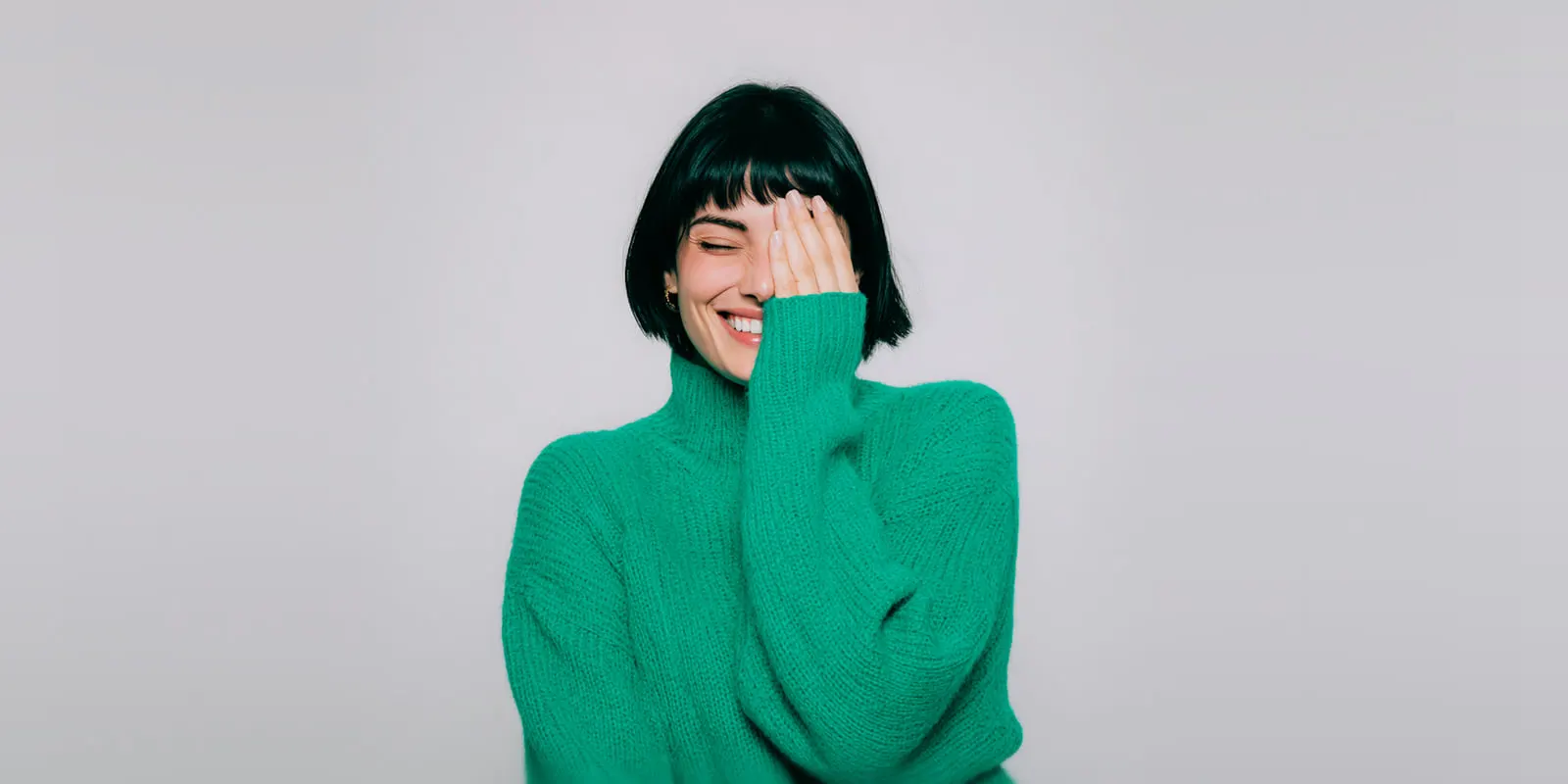 Woman with a black bob in a green knit sweater laughs on a gray backdrop, the on-model shot a brand may need as its final image