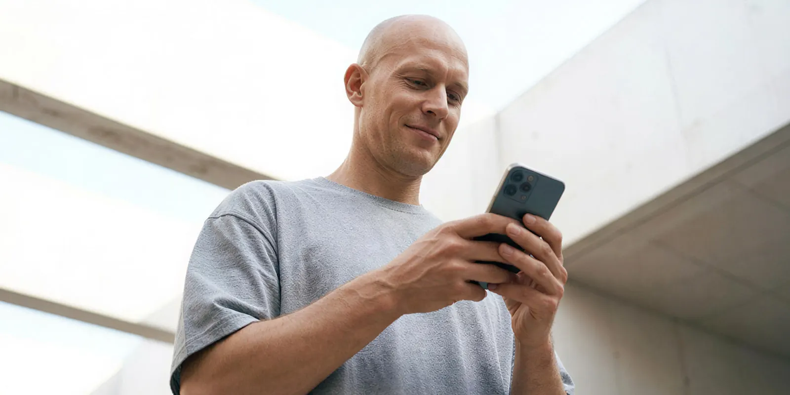 Man in a grey T-shirt smiling at a phone held upright in both hands, the vertical screen where a short clip has seconds to land