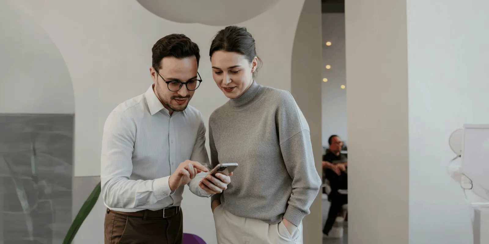 A man in glasses and a woman in a gray sweater read a post on one phone in a bright office, the check nobody can run on every partner post