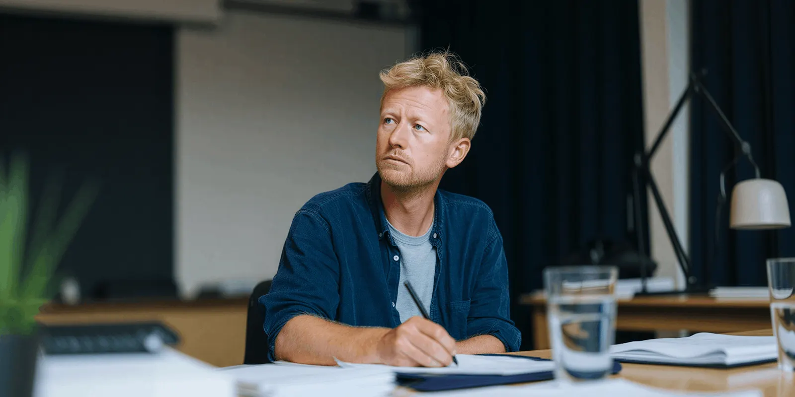 A man writes notes at a desk beside a lamp, the written list of edits a batch needs before it runs