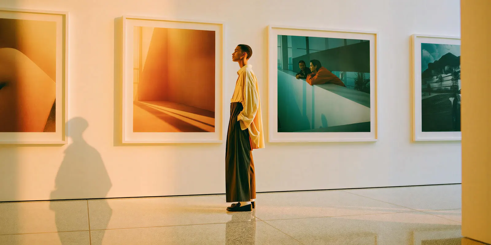 Person in a yellow shirt studying large framed photographs in a bright gallery, where every picture on show was chosen