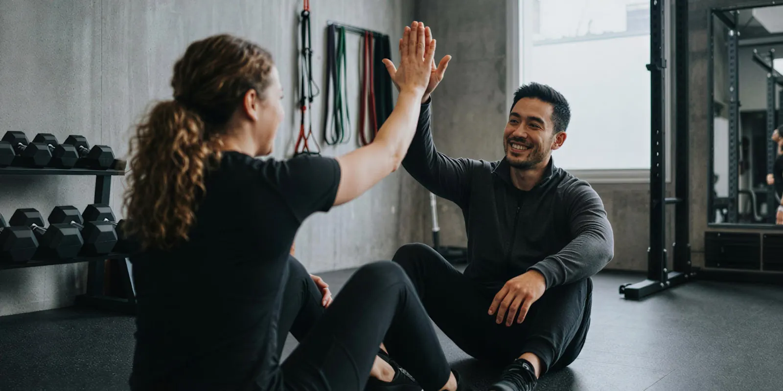 Two people in dark training clothes sharing a high five on a gym floor, a hand-contact moment to check frame by frame in any video clip
