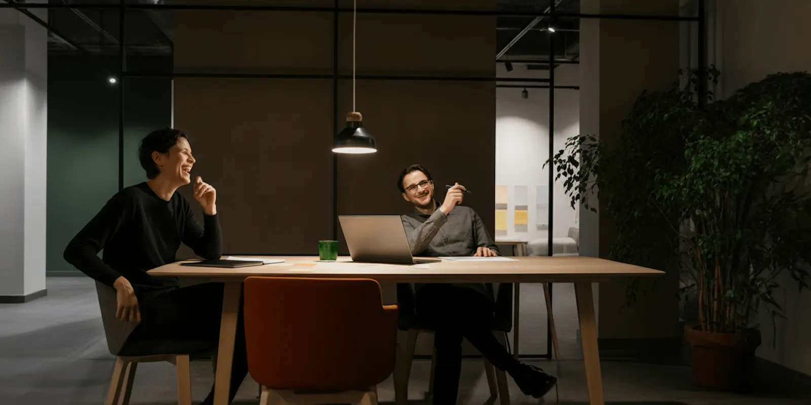 Two colleagues talk across an office table with a laptop open, agreeing on the store rules they want to run on their own