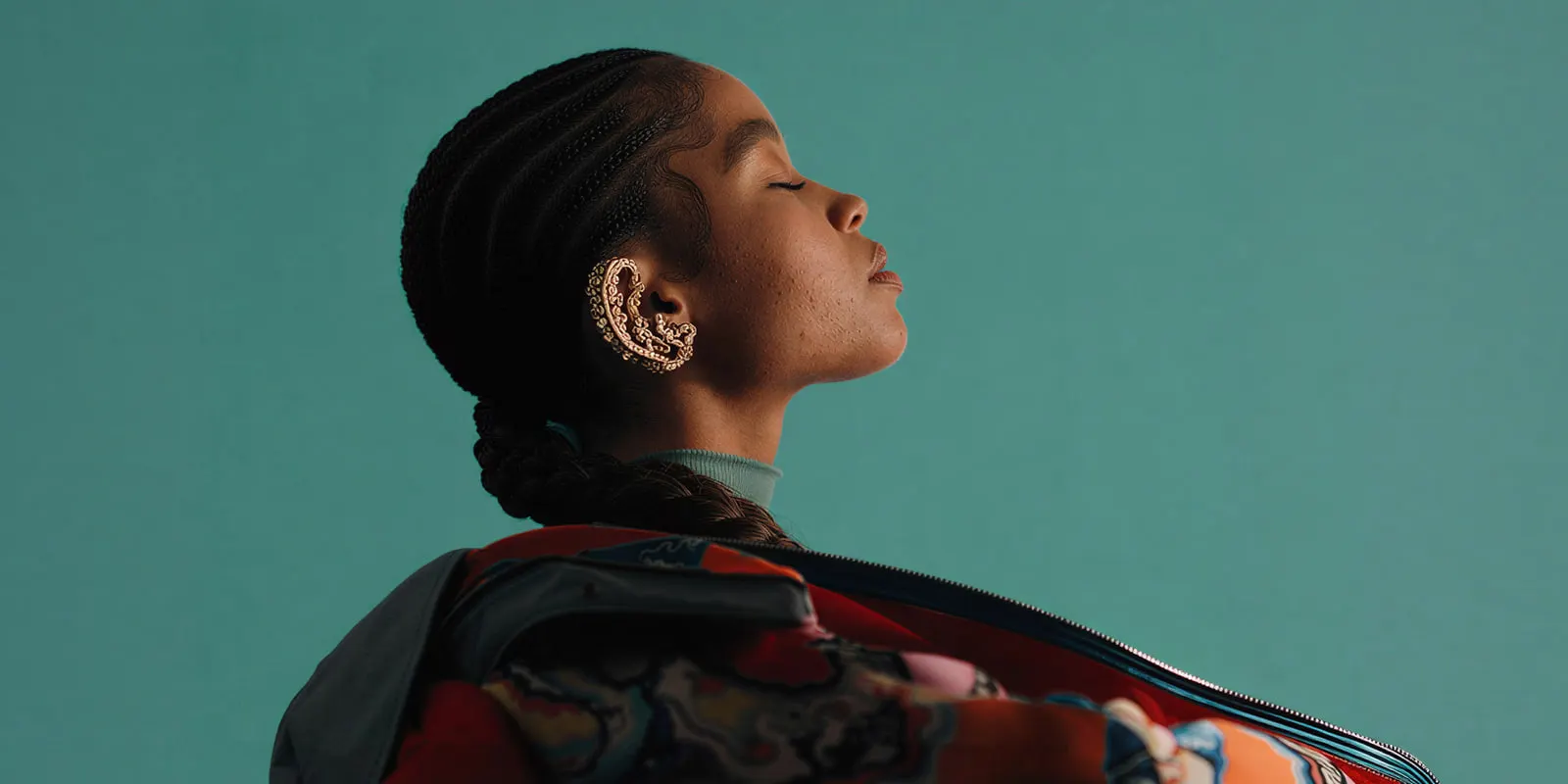 Woman with braided hair wearing a gold ear cuff against a teal backdrop, the worn shot that does the selling