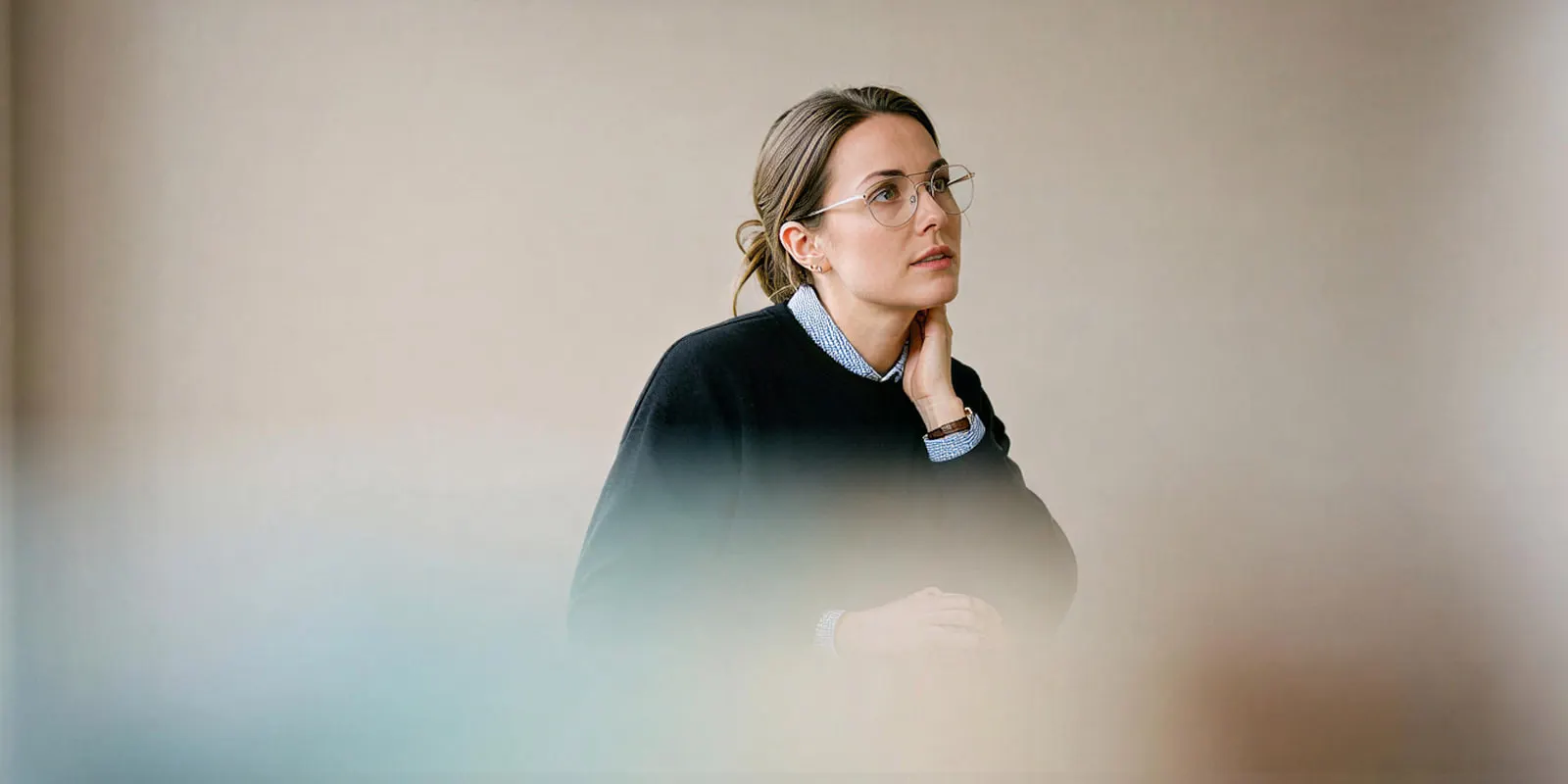 A woman in glasses and a navy sweater rests her chin on her hand in thought, deciding whether to reject a weak ad or edit it