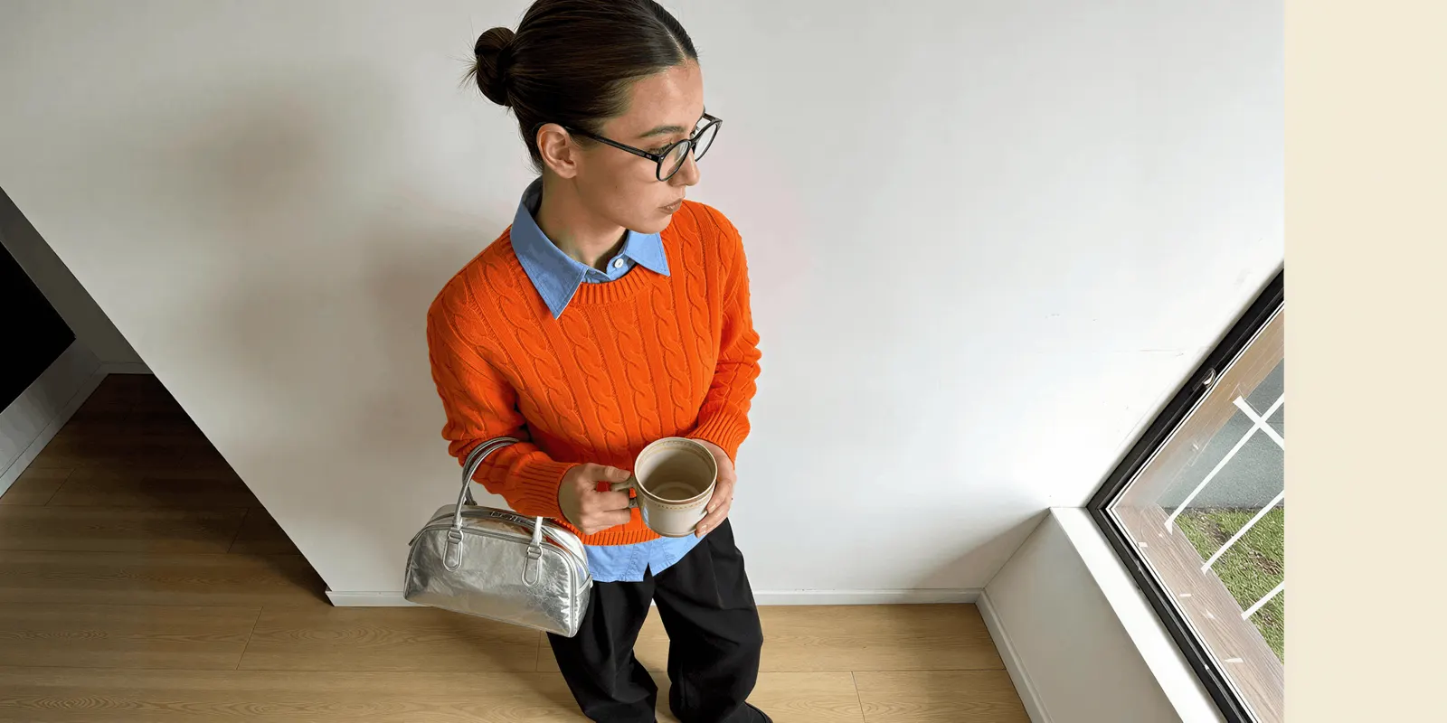 Overhead view of a woman in an orange sweater holding a silver handbag, a product whose shape and finish the source photo has to record