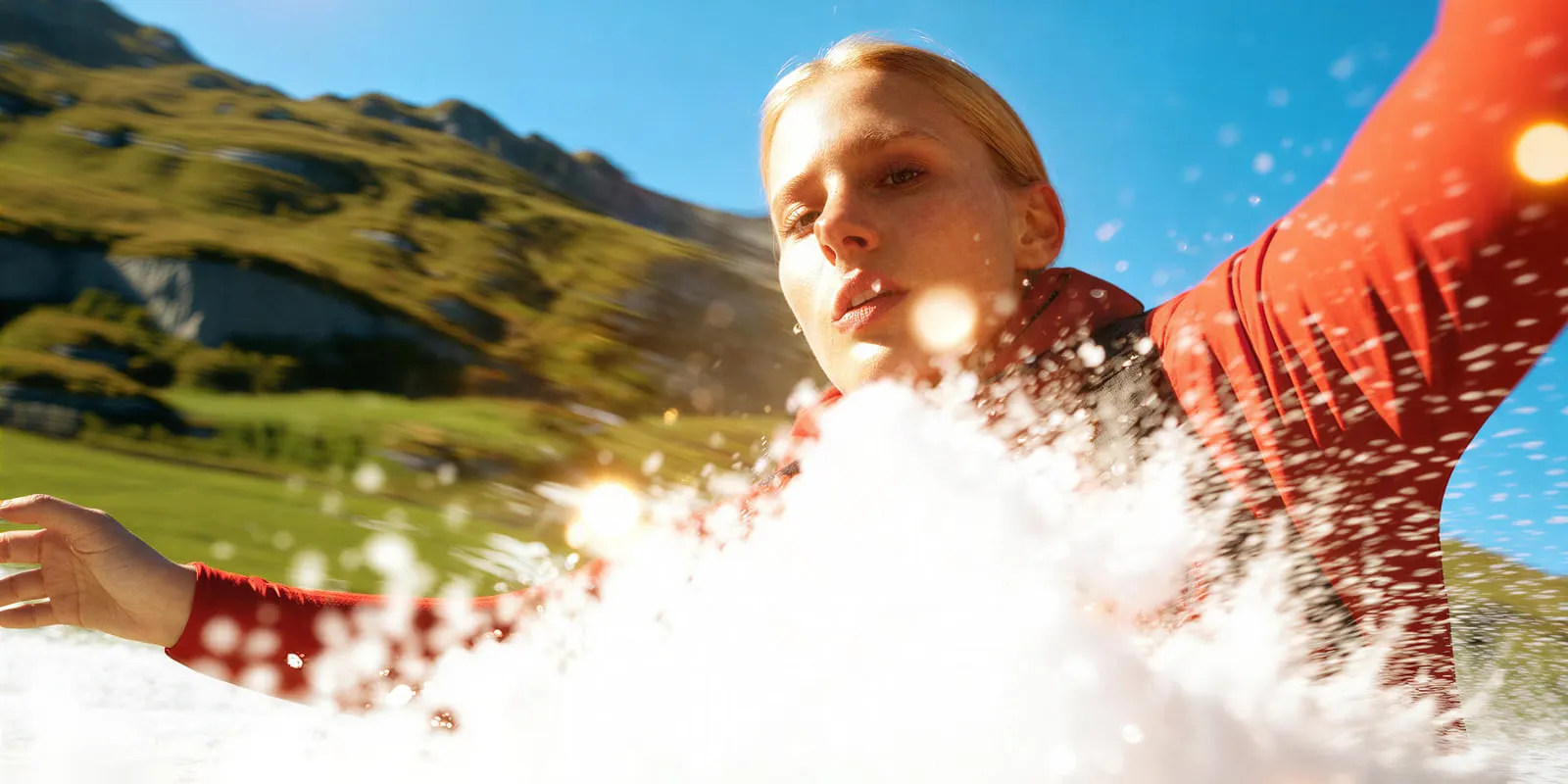 Woman in a red top under hard midday sun with water spraying toward the lens, the light that flattens detail on swim fabric