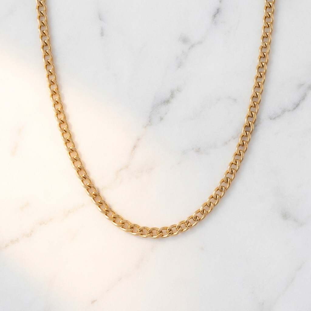 Gold chain necklace laid in an even curve on polished white marble, photographed straight down from above