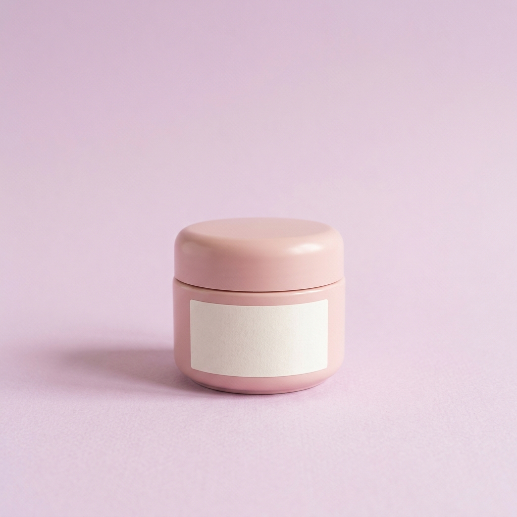 Soft pink ceramic cosmetic jar with a blank label, centred on pale lilac paper under even daylight.
